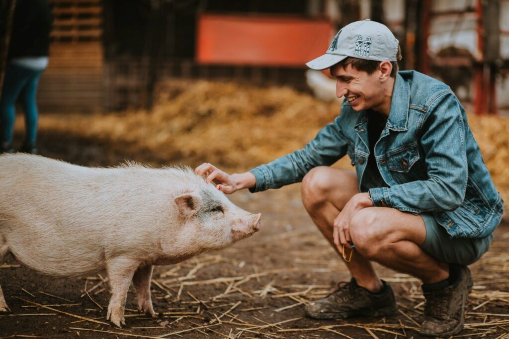 Eric is kneeling down and petting a pig.